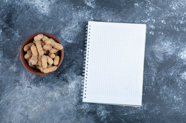 Houten kom van organische gepelde pinda's met leeg notitieboekje.