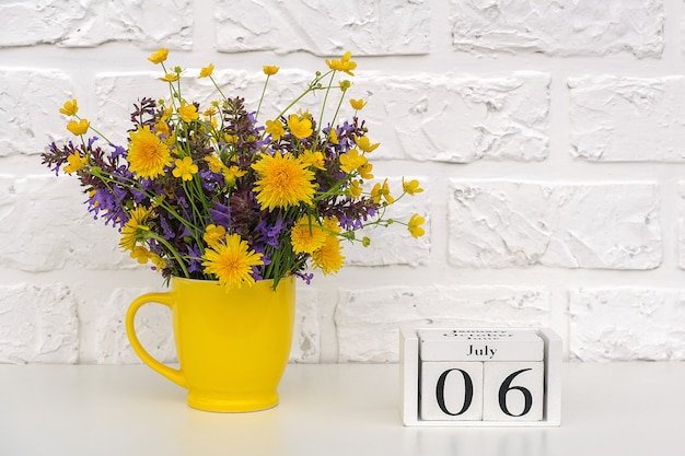 Houten kubuskalender 6 juli en gele beker met felgekleurde bloemen