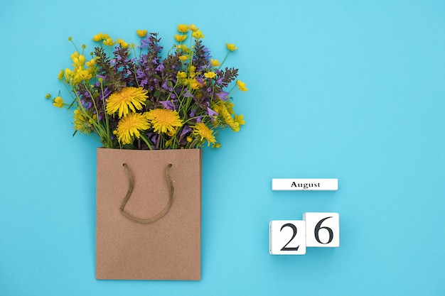 Houten kubussen kalender 26 augustus en veld kleurrijke rustieke bloemen in ambachtelijke pakket. Wenskaart