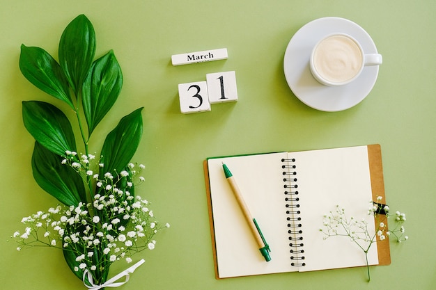 Houten kubussen kalender 31 maart. Kladblok, kopje koffie, boeket bloemen op groene achtergrond. Concept hallo lente Bovenaanzicht Plat lag Mock up