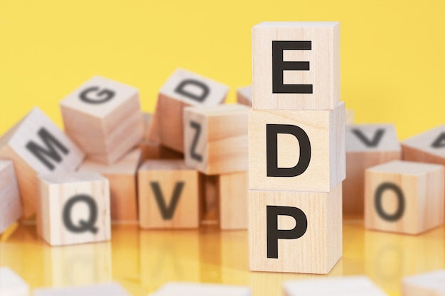 Houten kubussen met letters EDP gerangschikt in een verticale piramide, gele achtergrond, reflectie van het oppervlak van de tafel, bedrijfsconcept, EDP - een afkorting voor elektronische gegevensverwerking