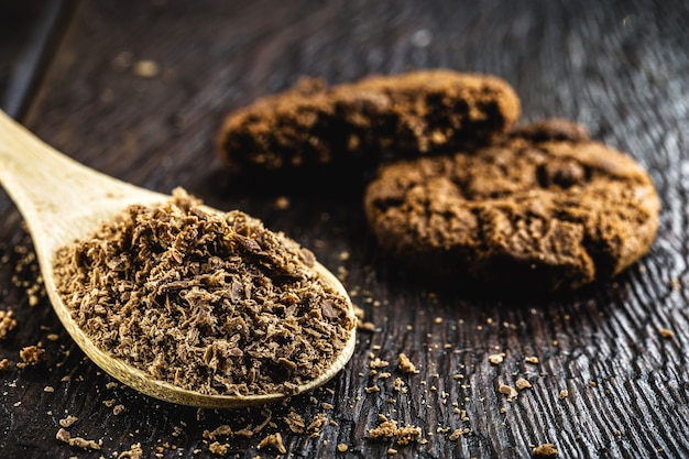 Houten lepel gebruikt in rustieke keuken, met poederchocolade. Rustieke houten tafel, zelfgemaakte chocoladekoekjes op de achtergrond