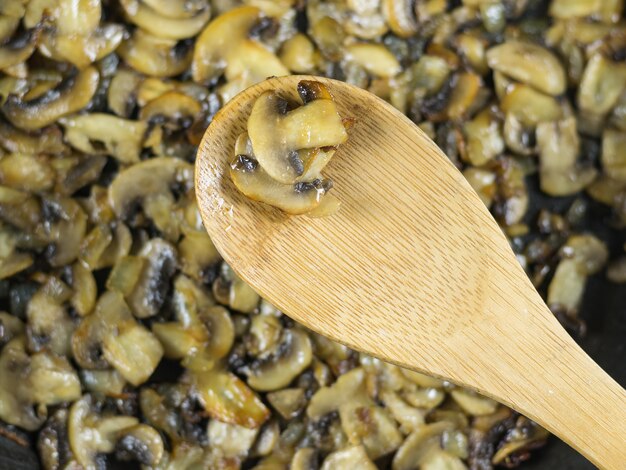 Houten lepel met champignons over pan gebakken champignons