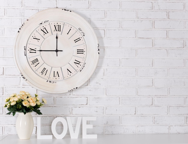 Houten letters vormen woord LOVE, bloemen en vintage klok over witte bakstenen muur achtergrond