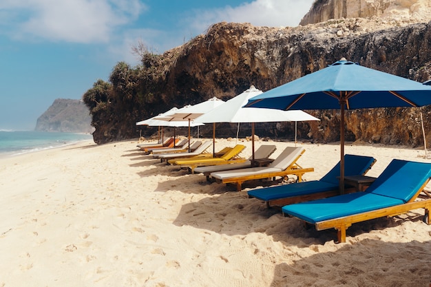 Houten ligstoelen met parasols langs de kustlijn.