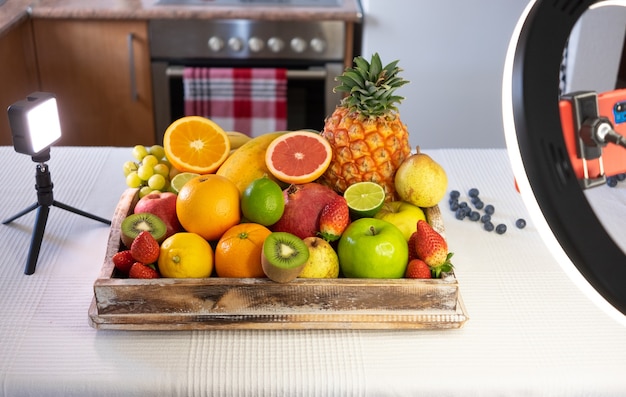 Houten mand vol met vers fruit op witte achtergrond. Citrus, papaya, ananas, aardbeien, granaatappel, bosbes. Verlichting en elektronische apparaten voor streaming