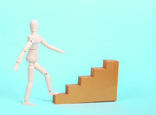 Houten marionet klimt de gouden trap tegen een blauwe achtergrond Carrière en persoonlijke groei concept