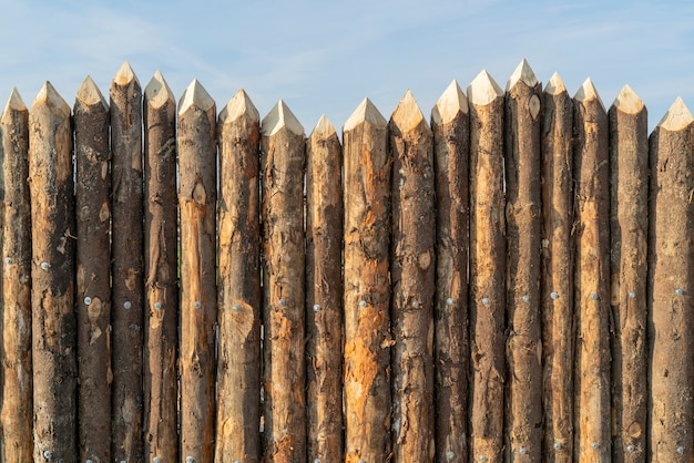 Houten palissade gemaakt van stammen. Log houten hek. Scherpe palen in de grond.