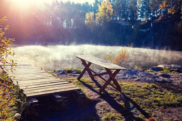 Houten pier en houten tafel aan het meer op een mistige herfstochtend