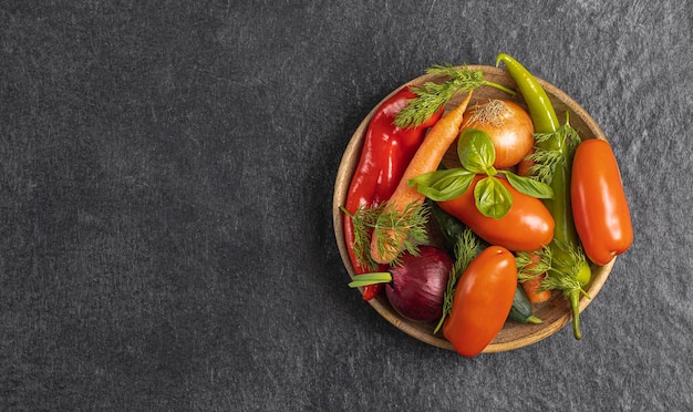 Houten plaat met verse groenten groene paprika tomaat ui wortel komkommer basilicum dille op grijze zwarte achtergrond bovenaanzicht