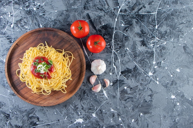 Houten plaat van heerlijke spaghetti met tomatensaus en groenten op marmeren oppervlak.