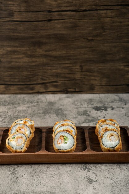 Houten plaat van tempura sushi rolt op stenen tafel.