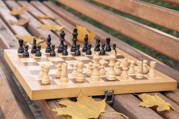 Houten schaakbord met stukken op de bank in een herfst stadspark. Ondiepe scherptediepte. Focus op de witte stukken.