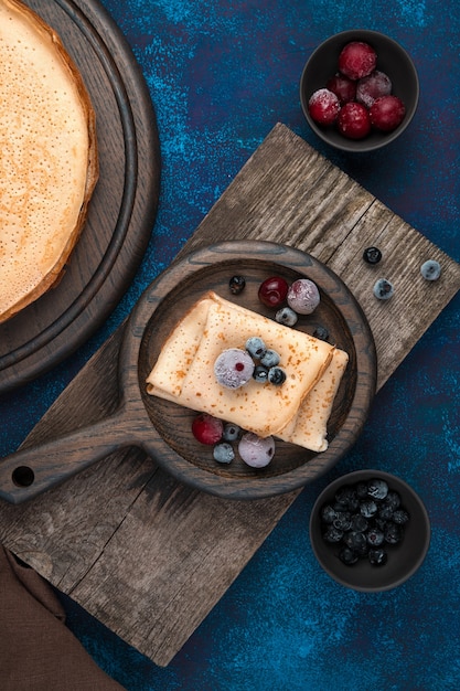 Houten schotel met pannenkoeken en bessen op een donkerblauwe achtergrond.