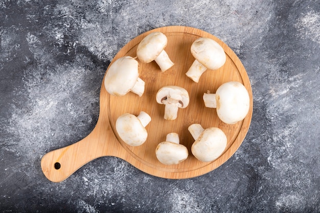 Houten snijplank van rauwe witte champignons op marmer.