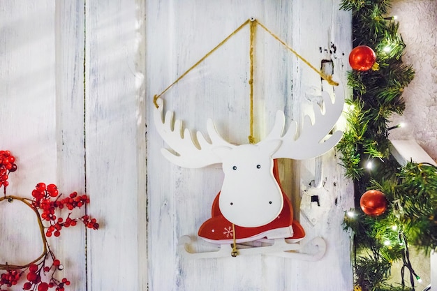 Houten speelgoed eland-elandschaatsen in een kerstmankostuum hangend aan een muur omringd door dennen- en lijsterbessentakken