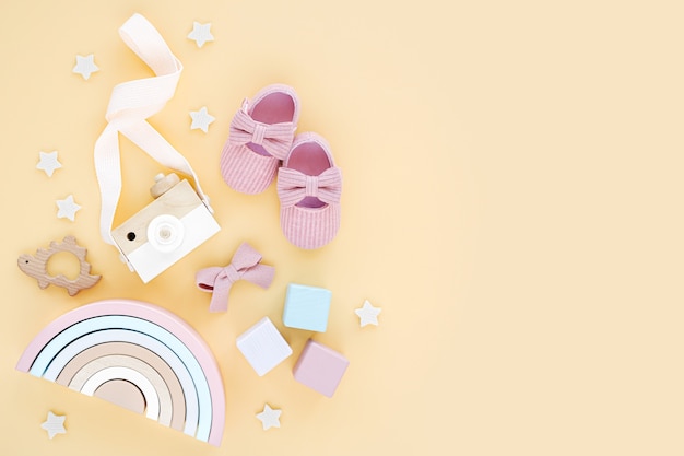 Houten speelgoed, roze pantoffels en regenboog voor pasgeboren meisje op gele achtergrond. Set babyspullen en accessoires. Platliggend, bovenaanzicht