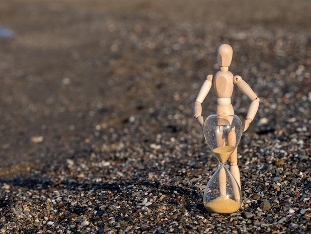 Houten stokfiguur naast zandloper op het strand aan de kust