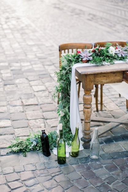 Houten tafel en stoelen versierd met bloemen, vetplanten en decor. Glazen flessen met kaarsen. Gedecoreerde tafel op de stenen bestrating in de oude stad Lviv