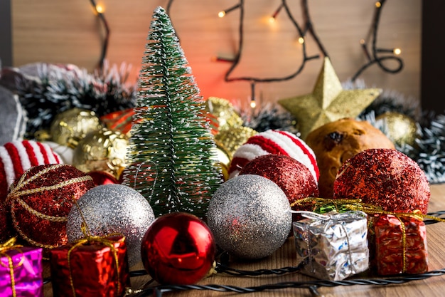 Houten tafel met kerstversiering. Rode, zilveren en gouden ballen, geschenkdozen, lichten, panettone, kerstboom en anderen. Selectieve aandacht.