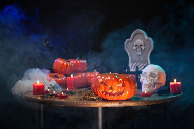 Houten tafel met rook en halloween decoratie erop. Spooky gesneden pompoen voor hallowee feest.