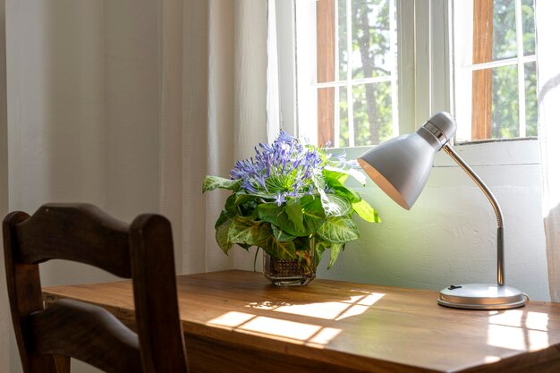 Houten tafel met stoellamp en een boeket bloemen bij het raam in een moderne werkruimte thuis