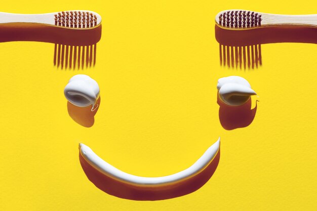 Houten tandenborstels en pasta op een gele achtergrond. Tandheelkundig concept in de vorm van een grappig gezicht.