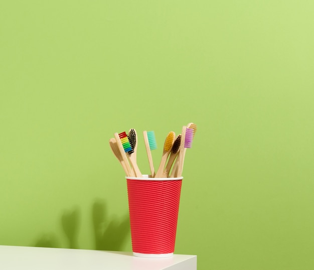 Houten tandenborstels in een papieren beker op een witte tafel. Groene achtergrond, geen afval
