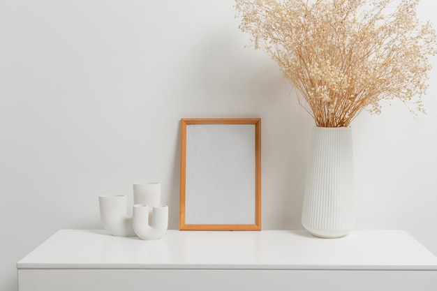 Houten verticaal frame met witte vaas met gipskruidbloemen over witte muur
