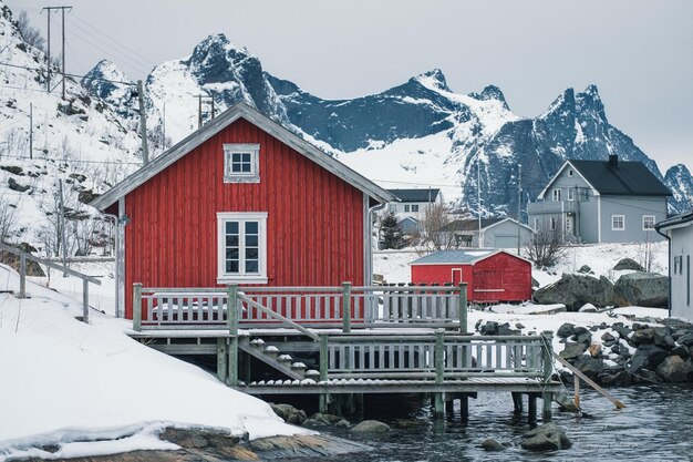 Houten vissershuisje rorbuer aan de kust omringd door besneeuwde bergen in de winter op de nordland lofoten-eilanden