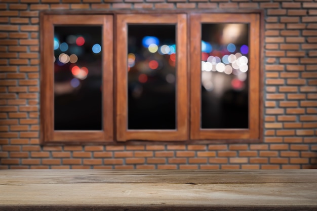 Houten vloer of tafel op houten ramen en bakstenen muur met nachtlicht van stadsachtergrond