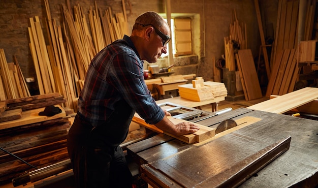 Houtsnijtafel met elektrische cirkelzaag Senior Professional timmerman in uniform snijden houten plank bij zagerij timmerwerk productie Zaagmachine