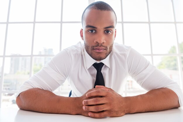 How can I help you? Confident young African man in shirt and tie holding hands clasped