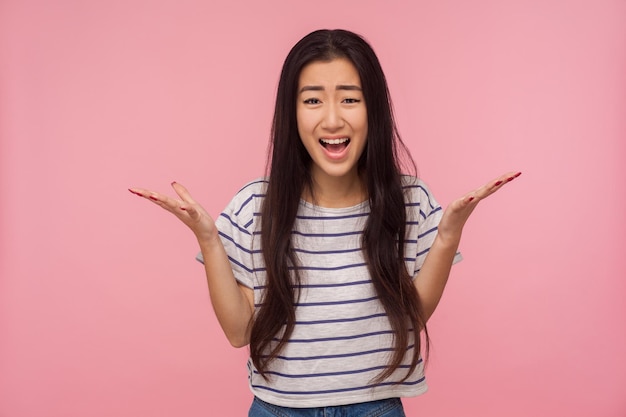 How could you Portrait of displeased girl with long hair in striped tshirt raising hands in questioning gesture quarreling asking what why with indignant expression indoor studio shot isolated