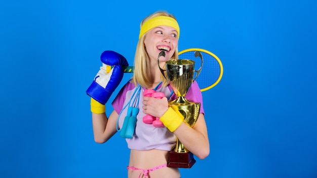 How to find time for everything sport equipment store sport for\
every day sport shop assortment girl successful modern woman hold\
golden goblet of sport champion and equipment blue background