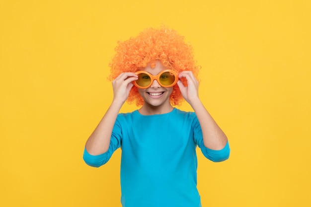How do i look cheerful teen girl wearing party glasses just having fun april fools day happy childhood going crazy fancy party look kid in curly clown wig funny child with fancy hair
