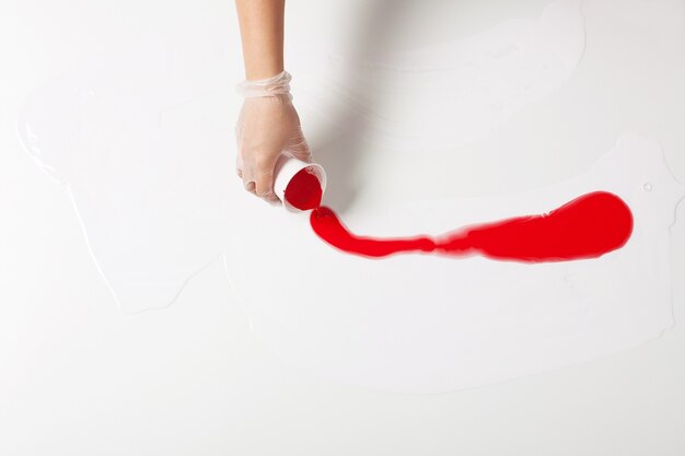 How to make acrylic painting. Work in progress. Female hand holding a plastic cup with red paint.