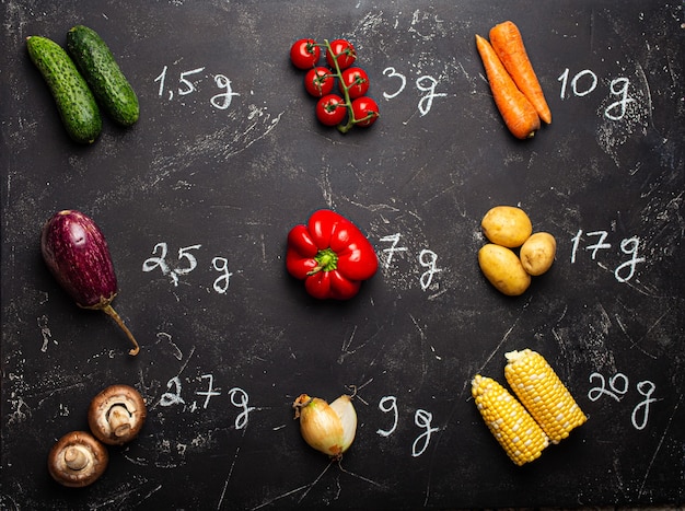 Photo how many carbohydrates in different vegetables chart, fresh veggies with chalk wrote carbohydrates quantity on black stone background top view. keto diet and low carb nutrition concept