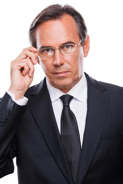 How may I help you? Portrait of confident mature man in formalwear adjusting his eyeglasses and looking at camera while standing against white background