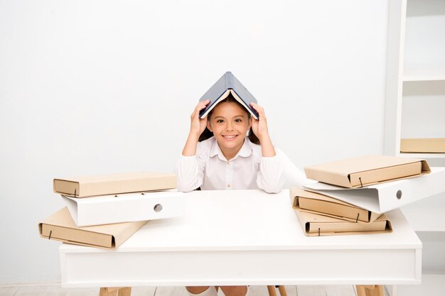 ポジティブであり続け、タスクを管理する方法。女の子の子供の本の屋根の頭の白い背景。女子高生は勉強を読んで前向きな笑顔を保ちます。子供の制服の笑顔。現実から隠れている女子高生。