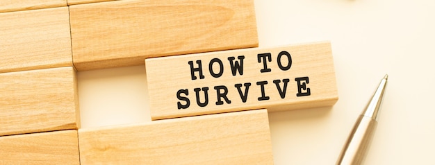 HOW TO SURVIVE text on a strip of wood lying on a white table with a metal pen.