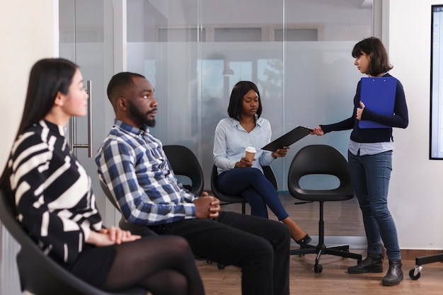 HR 부서 관리자는 마케팅 회사 로비 구역에서 기다리는 동안 아프리카계 미국인 여성 취업 지원서를 제공합니다. 사업가로부터 문서 클립보드를 받는 실업자.
