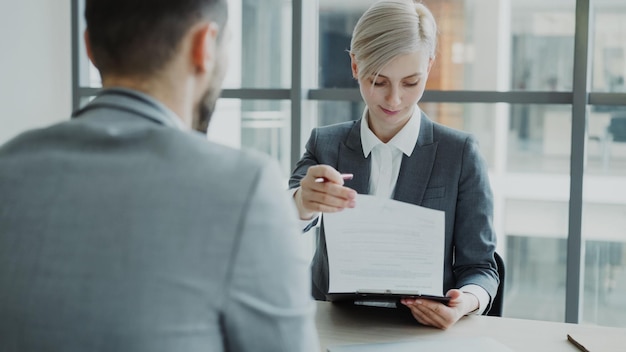 HR-zakenvrouw met sollicitatiegesprek met jonge man in pak en kijken naar zijn cv-aanvraag