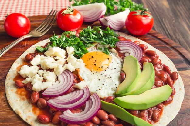 Huevos rancheros colazione pizza con pomodori, cipolla e prezzemolo su tavola in legno rustico. messa a fuoco selettiva.