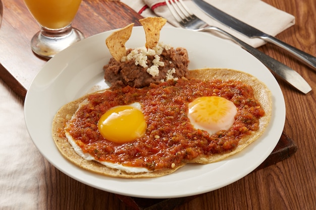 Huevos rancheros con salsa picante roja y frijoles refritos desayuno tipico mexicano