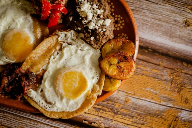 Huevos rancheros, 고기, 콩 및 튀긴 질경이를 점토 접시에 담습니다. 전형적인 멕시코 음식.