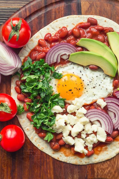 Huevos rancheros ontbijtpizza met tomaten, ui en peterselie op rustieke houten ondergrond. Bovenaanzicht.