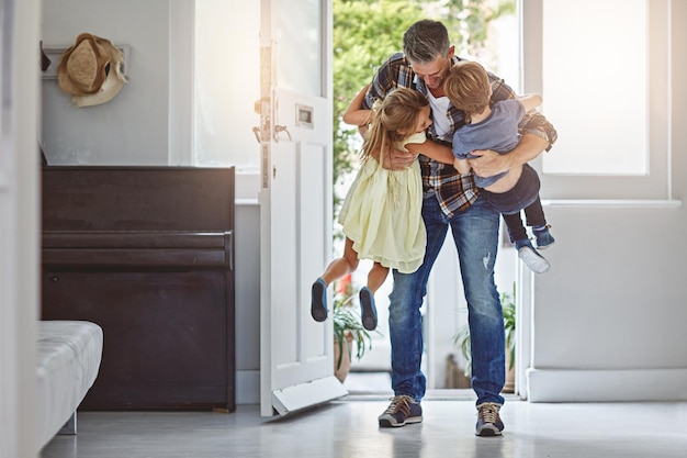 Hug welcome and a father with children at front door greeting after work and excited to be home Happy family and a dad hugging a girl and boy kid after arriving from a job with love in a house