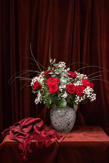 A huge bouquet of red roses with white flowers on a dark brown fabricStill life