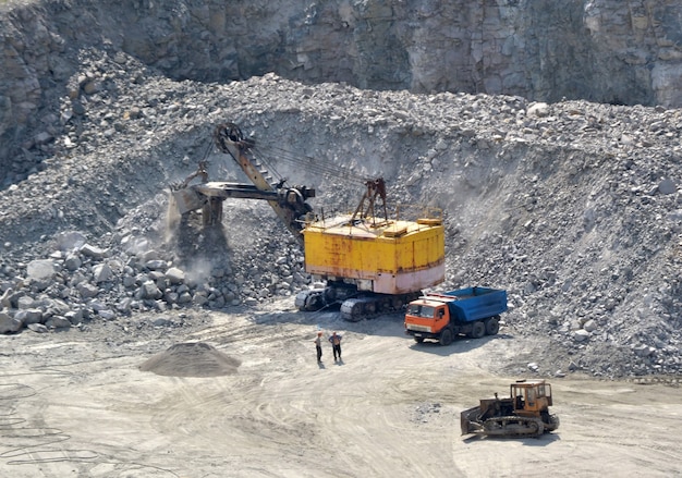 Huge excavator, truck and man standing next on granite quarry